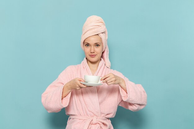 파란색에 미소로 커피를 마시는 샤워 후 분홍색 목욕 가운에 젊은 여성