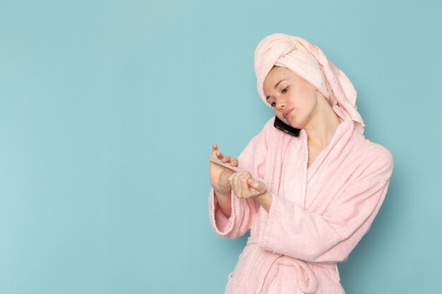 young female in pink bathrobe after shower fixing her nails on blue