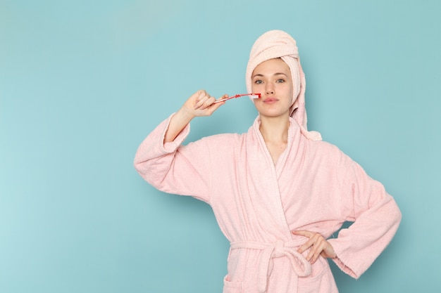 young female in pink bathrobe after shower holding toothbrush on blue