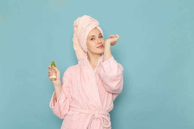 young female in pink bathrobe after shower holding and using spray on blue