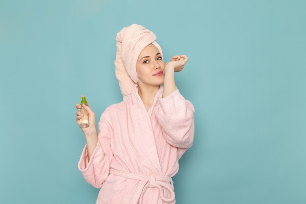 シャワーを押しながらブルーにスプレーを使用した後のピンクのバスローブの若い女性