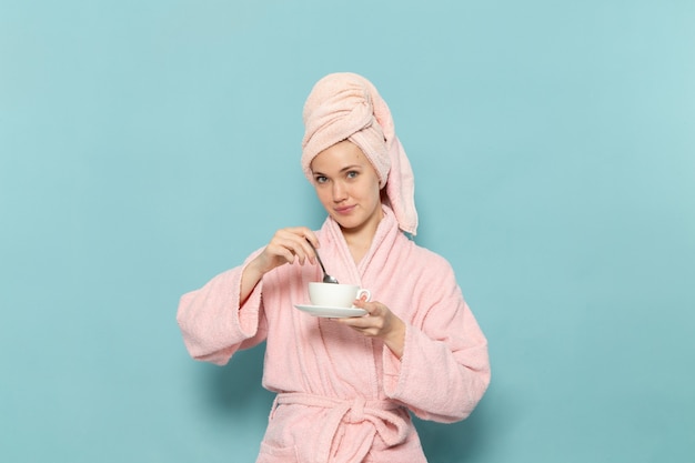 ブルーのコーヒーを混ぜるシャワー後のピンクのバスローブの若い女性