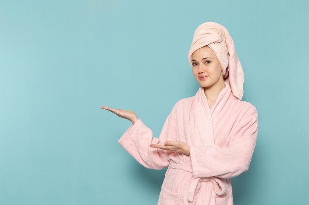 young female in pink bathrobe after shower smiling and posing on blue