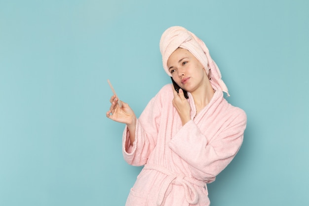 молодая женщина в розовом халате после душа разговаривает по телефону на синем