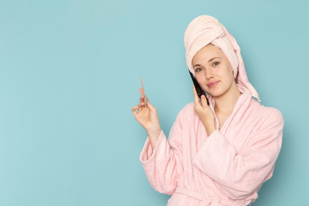 young female in pink bathrobe after shower talking on phone on blue