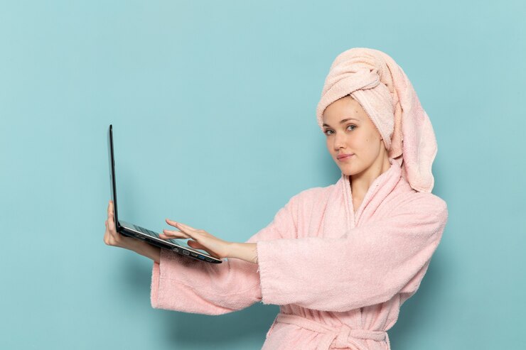Free Photo young female in pink bathrobe after shower using black laptop on blue
