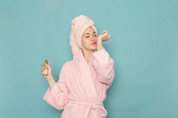 young female in pink bathrobe after shower using spray on blue