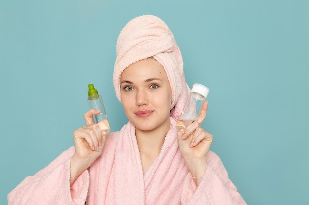 young female in pink bathrobe holding make-up flasks on blue