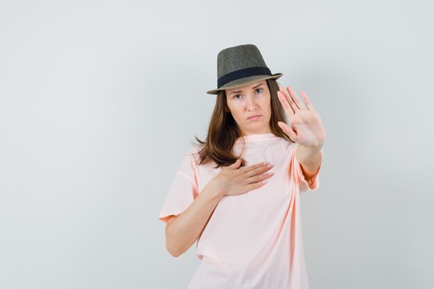 Young female in pink t-shirt, hat showing refusal gesture and looking serious , front view.