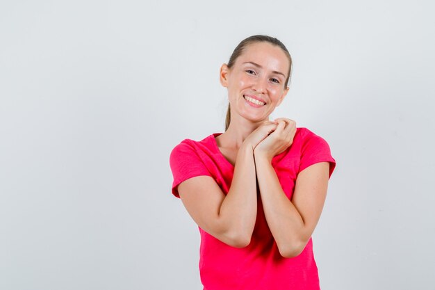 Young female in pink t-shirt holding clasped hands and looking cute , front view.