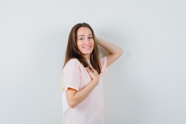 Молодая женщина в розовой футболке позирует, стоя и глядя весело, вид спереди.