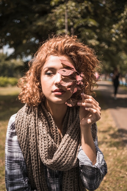 Молодая женщина в клетчатой ​​рубашке, держащей малиновый лист в парке