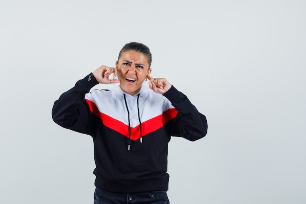 Young female plugging ears with fingers in colorful sweatshirt and looking bored. front view.