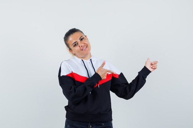 Young female pointing aside in colorful sweatshirt , front view.