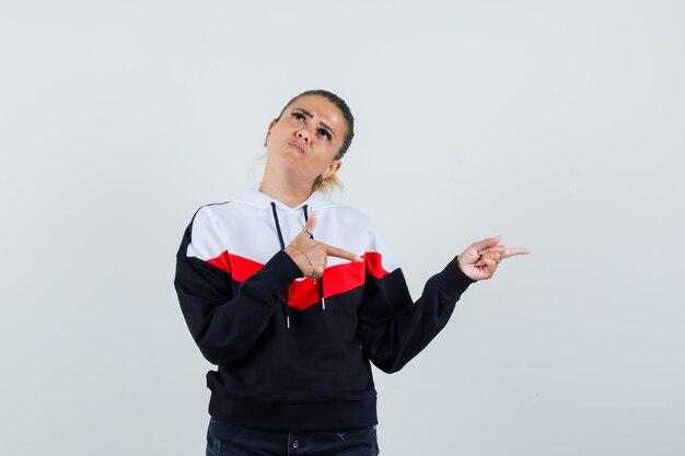 Young female pointing aside in colorful sweatshirt and looking stubborn. front view.