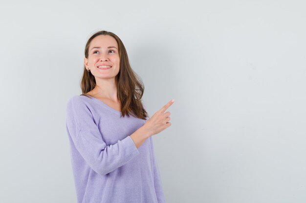 Young female pointing aside in lilac blouse and looking glad 