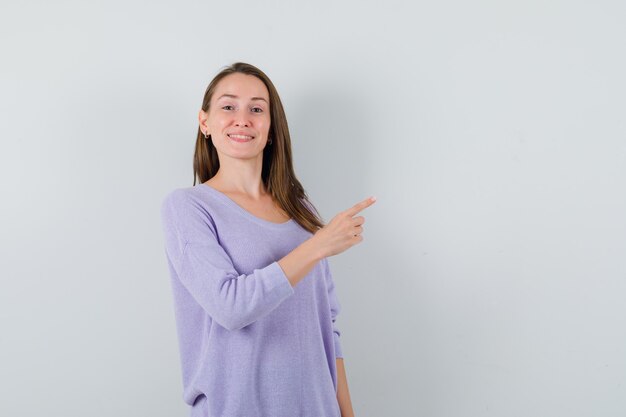 Young female pointing aside in lilac blouse and looking pleased 