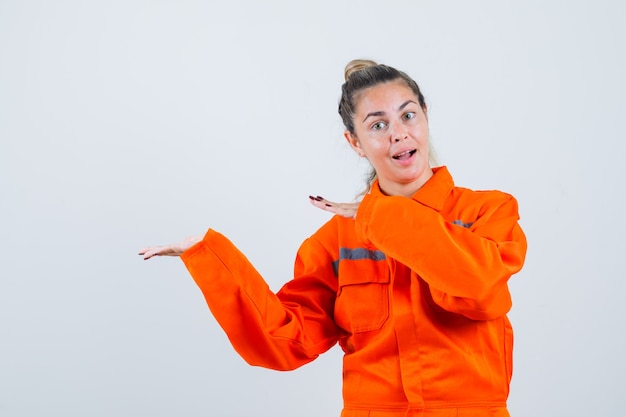 Young female pointing aside to show something in worker uniform and looking positive. front view.