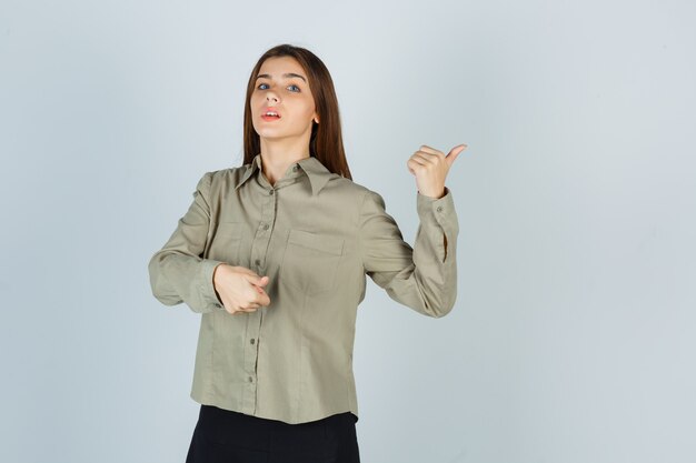 Foto gratuita giovane femmina che indica da parte con i pollici in camicia, gonna e sguardo indeciso