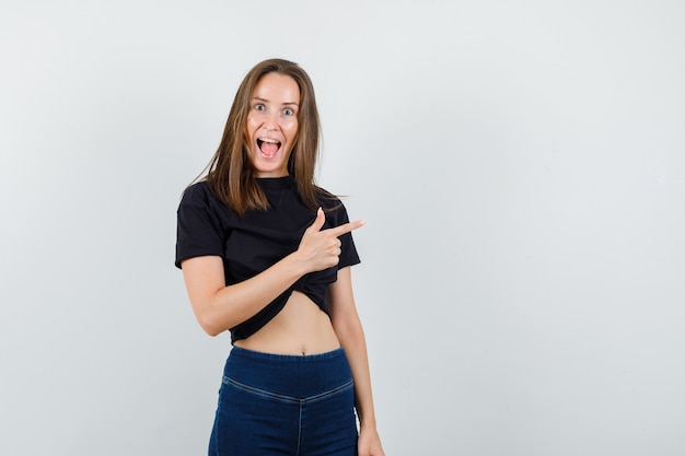 Young female pointing away in black blouse, pants and looking happy.