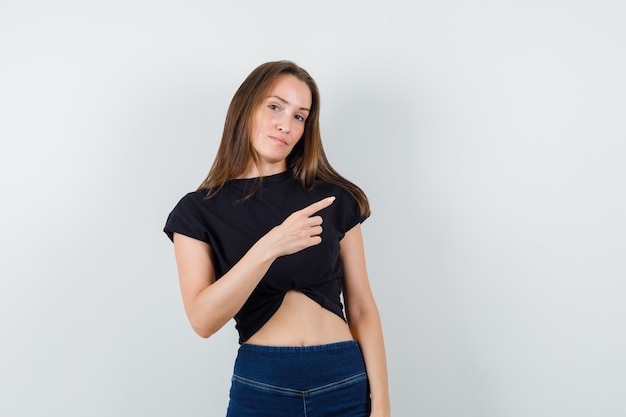 Young female pointing away in black blouse, pants and looking positive