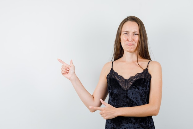 Foto gratuita giovane donna che punta lontano in canottiera nera e sembra malinconica