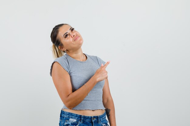 Young female pointing away in t-shirt, shorts and looking pensive. 