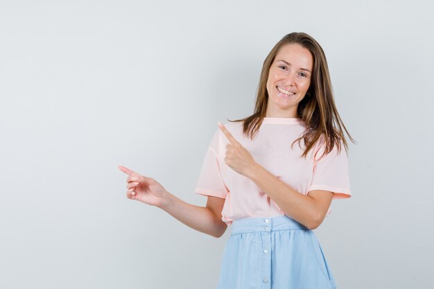 Young female pointing away in t-shirt, skirt and looking optimistic , front view.