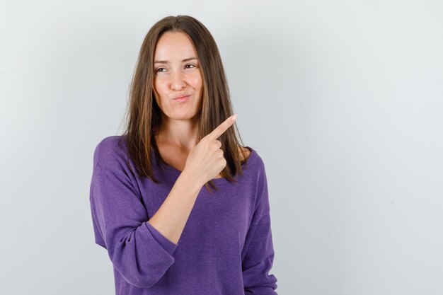 Young female pointing away in violet shirt and looking pensive. front view.