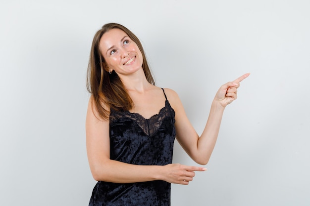 Young female pointing away while looking up in black singlet and looking cheerful.