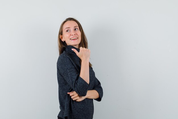 Young female pointing away with thumb in shirt and looking hopeful. front view.