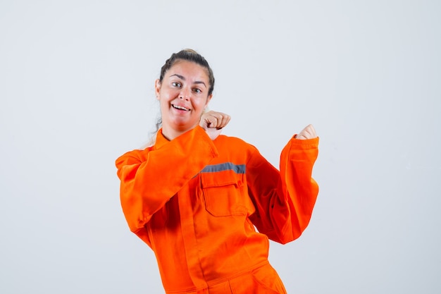 Foto gratuita giovane donna che punta indietro in uniforme da lavoratore e guardando divertito, vista frontale.