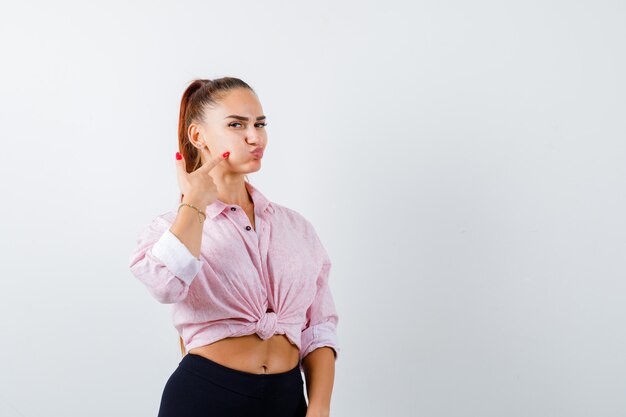 Young female pointing at blown cheek in casual shirt and looking cute , front view.