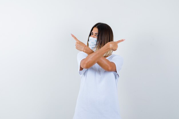 Young female pointing both corners in t-shirt, mask and looking hesitant. front view.