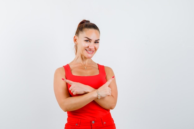 Young female pointing to both sides in red tank top, pants and looking happy , front view.