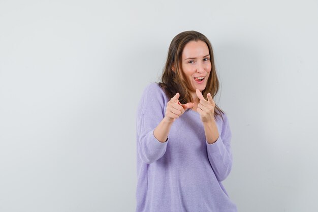 Young female pointing at camera in lilac blouse and looking crazy 