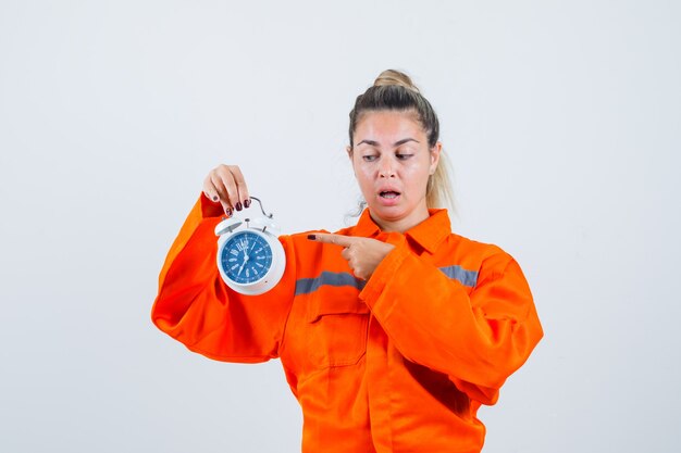 Young female pointing at clock in worker uniform and looking focused. front view.