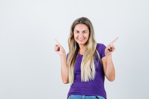 Young female pointing at different sides in violet t-shirt and looking jolly. front view.