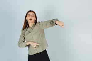 Free photo young female pointing down in shirt, skirt and looking focused. front view.