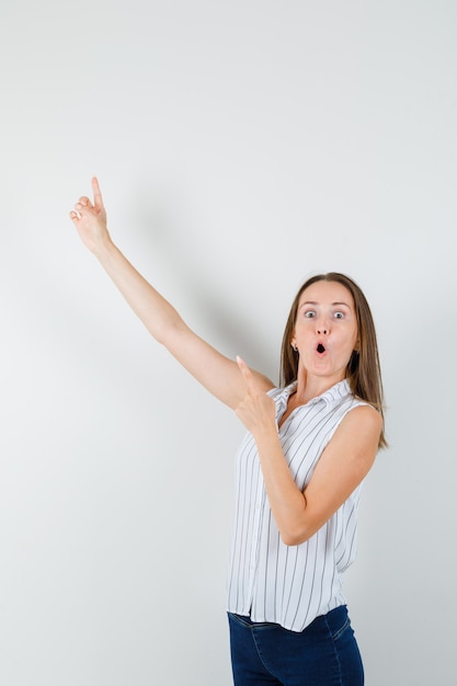 Young female pointing fingers up in t-shirt, jeans and looking amazed. front view.