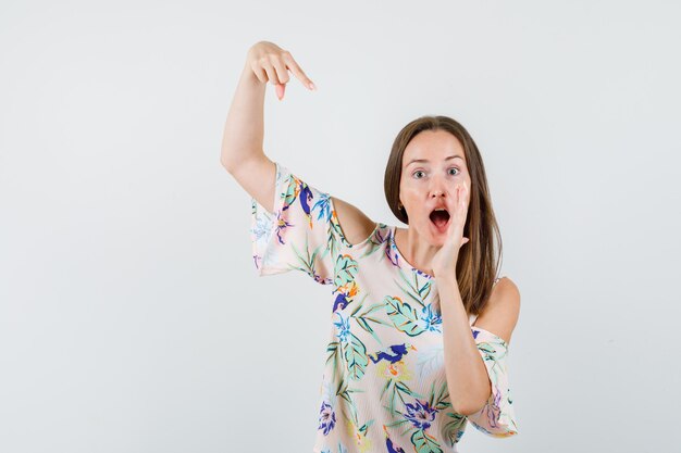 Young female pointing at her raised palm in shirt , front view.