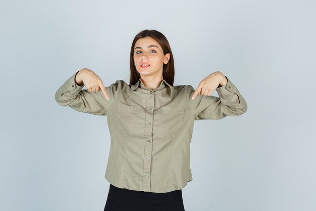 Young female pointing at herself in shirt, skirt and looking proud , front view.