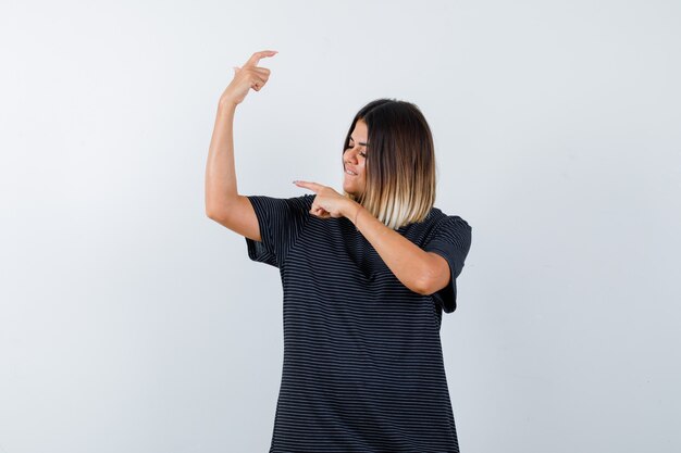 Young female pointing at muscles of arm in polo dress and looking proud. front view.