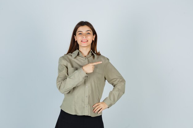 Young female pointing right in shirt, skirt and looking merry