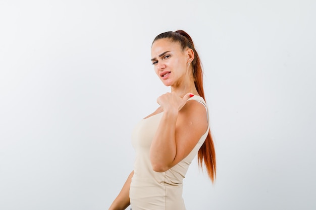 Free photo young female pointing to the right side with thumb in beige tank top and looking confident , front view.