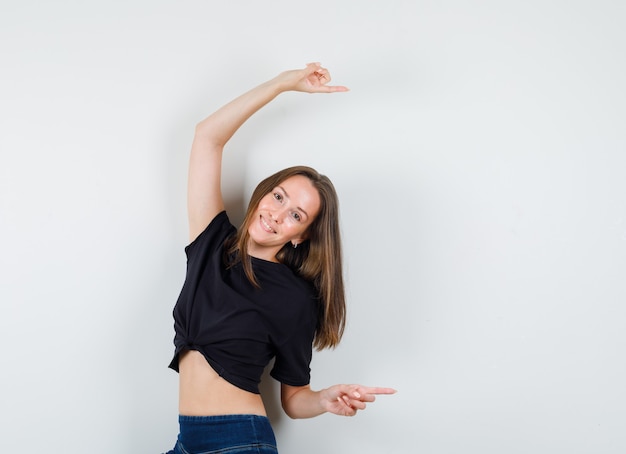 Foto gratuita giovane donna che punta al lato in camicetta nera, pantaloni e sembra allegra.