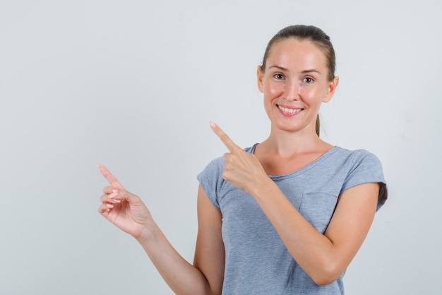 Young female pointing to side in grey t-shirt and looking cheery. front view.