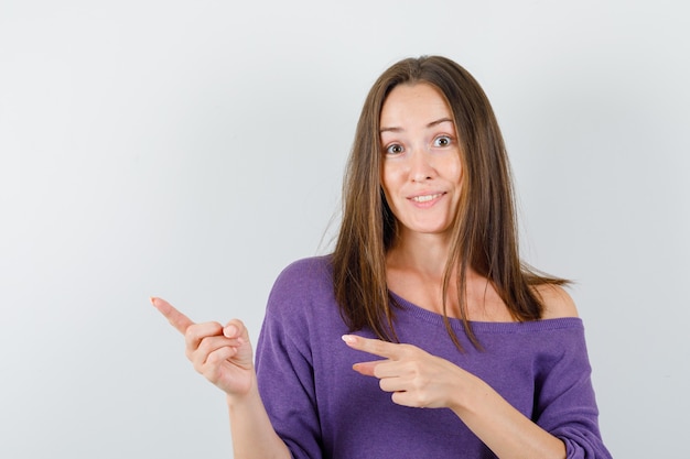 Young female pointing to side in violet shirt and looking helpful , front view.