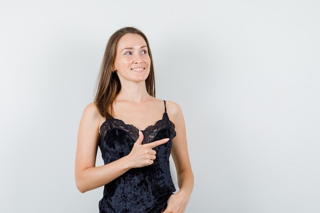 Free photo young female pointing to side while looking up in black singlet and looking positive.