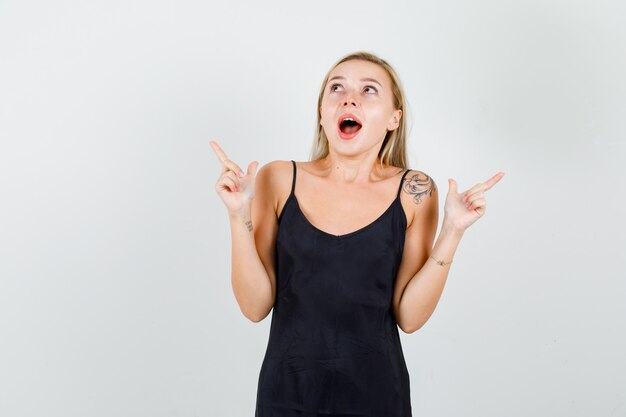 Young female pointing to side with gun gesture in black singlet and looking surprised 